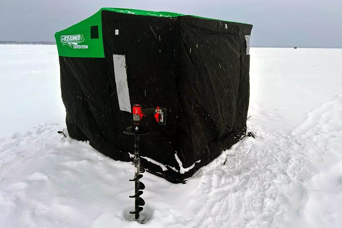 A black and green portable ice-fishing house with a power auger leaning against it.
